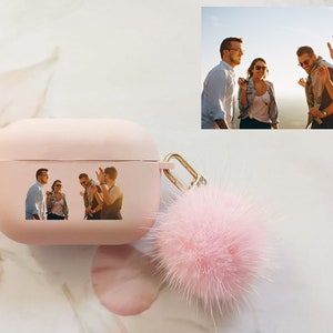 May include: Pink Airpods case with a fuzzy pink pom-pom keychain. The case has a photo of four friends laughing together.