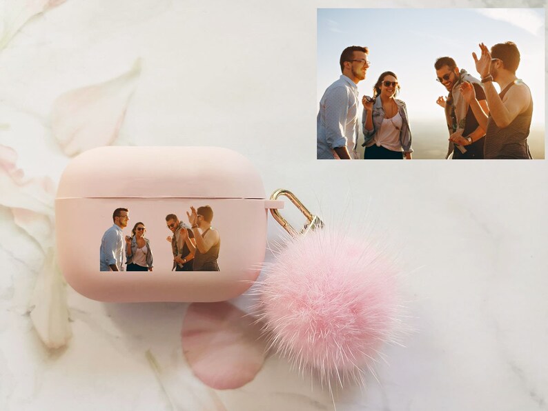 May include: Pink Airpods case with a fuzzy pink pom-pom keychain. The case has a photo of four friends laughing together.
