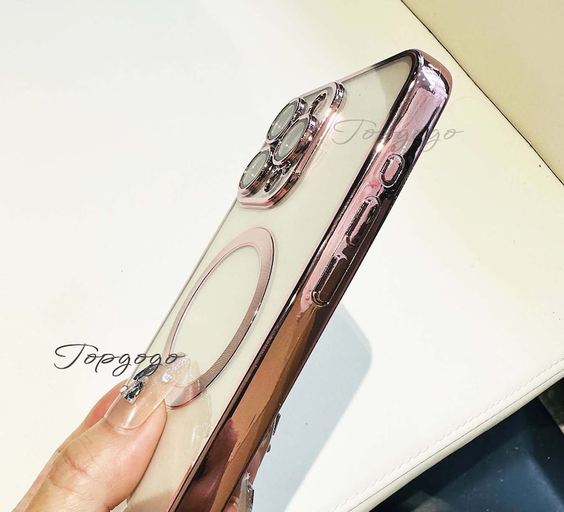 Puede incluir: Una funda para tel&eacute;fono de color rosa dorado con la parte posterior transparente y un soporte para anillo. La funda tiene una protuberancia de c&aacute;mara elevada con un dise&ntilde;o decorativo.