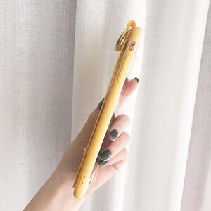 May include: A yellow phone case with a gold ring attached. The case is clear on the back and has a raised camera bump.