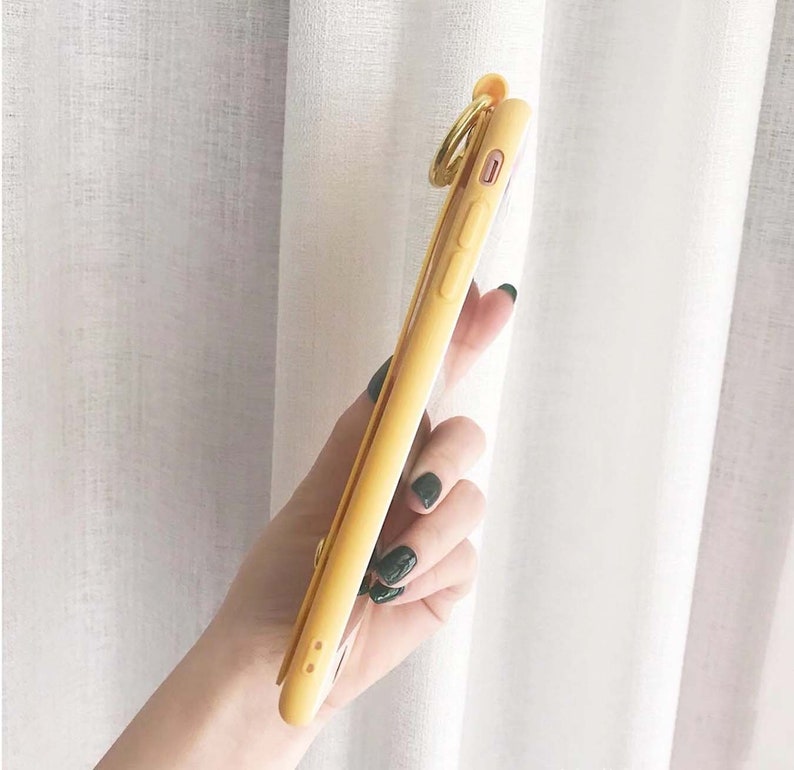 May include: A yellow phone case with a gold ring attached. The case is clear on the back and has a raised camera bump.