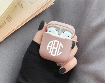 Könnte beinhalten: Eine rosa Silikonhülle für kabellose Ohrhörer mit einem weißen Monogramm "ABC" auf der Vorderseite.