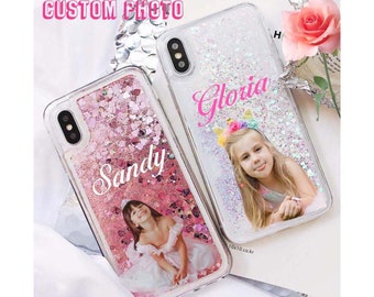 Puede incluir: Dos fundas transparentes para teléfono con purpurina y una foto de un niño dentro. La funda de la izquierda tiene purpurina rosa y el nombre "Sandy" escrito en ella. La funda de la derecha tiene purpurina blanca y el nombre "Gloria" escrito en ella.