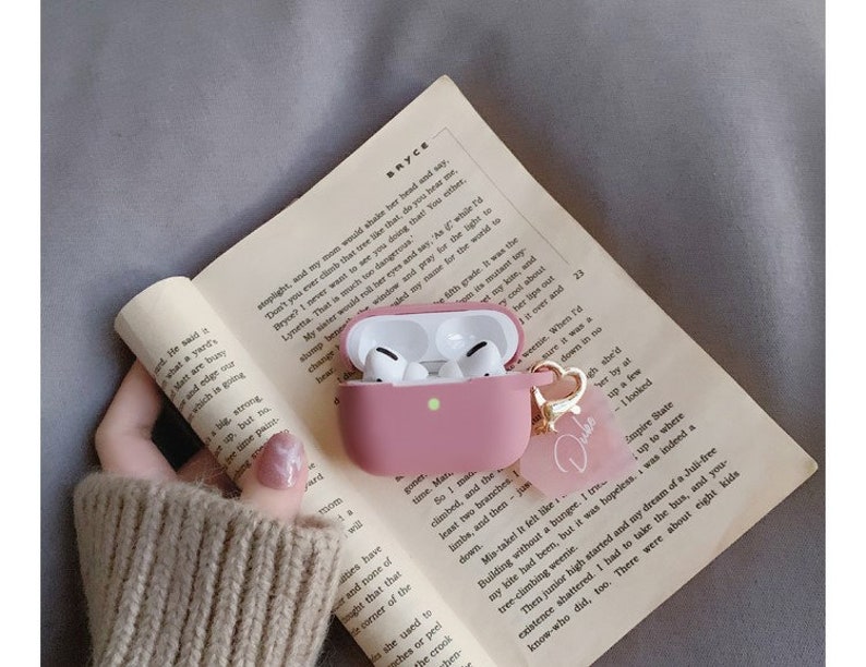 May include: A pink protective case for wireless earbuds with a gold charm that says "Dube". The case is open and the earbuds are visible inside.