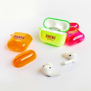 K&ouml;nnte beinhalten: Drei transparente Plastikh&uuml;llen f&uuml;r kabellose Ohrh&ouml;rer, eine ist gr&uuml;n mit dem Text "XMENG 1999.06.01", eine ist pink mit dem Text "SALLIE 2000.07.22" und eine ist orange mit dem Text "RAMYA 1998.07.22". Zwei wei&szlig;e kabellose Ohrh&ouml;rer sind ebenfalls abgebildet.