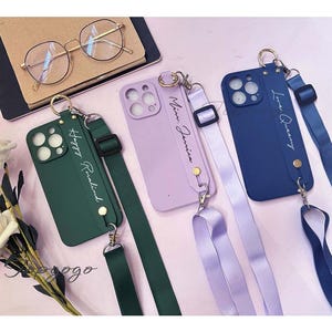 May include: Three phone cases with matching straps. The cases are green, purple, and blue. Each case has a different name written on it: "Happy Rosalind", "Mia Jamison", and "Love Queeny".