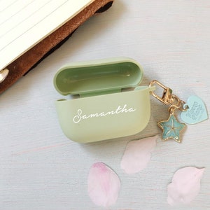 May include: A light green Airpods case with the name Samantha written in white on the front. The case has a gold charm attached to it with a blue starfish and a heart that says "More Than Words".