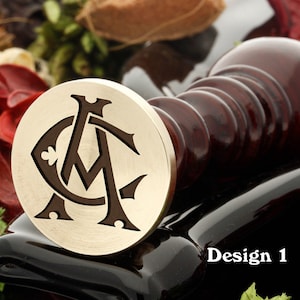 May include: A brass wax seal stamp featuring a design of two intertwined letters, "A" and "C", with a clover leaf at the centre. The stamp is on a black surface with a wooden handle.