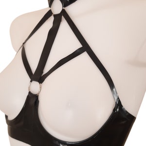 Side view of The Image shows a black open cup bra base with open cups, straps to frame the outside of the boobs with a central strap between leading up to a connecte4d choker. 2 silver tone O rings connect the bra band with the harness part.