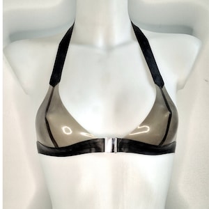 Peut inclure: Un soutien-gorge style dos-nu en latex gris translucide avec des bordures noires opaques le long de l'encolure, des bretelles et de la bande sous la poitrine. Le vêtement présente une fermeture centrale à clip en métal argenté sur le devant.