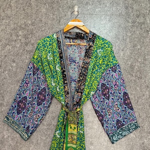 May include: A colourful patterned kimono robe in green, blue, and purple. The robe has a paisley and floral design, with a matching belt. The sleeves are wide and the robe is hanging on a wooden hanger.