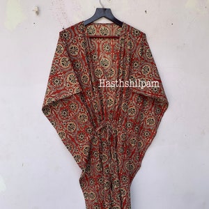 May include: A long, red and cream colored kaftan with a floral print. The kaftan has a deep V-neck and a tie at the waist. The text "Hasthshilpam" is printed on the front of the kaftan.