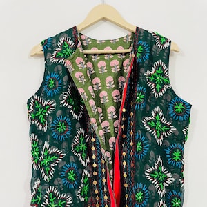 Peut inclure: Un gilet sans manches vert foncé avec un imprimé floral et des accents dorés. Le gilet est ouvert à l'avant, révélant une doublure florale rose et verte.
