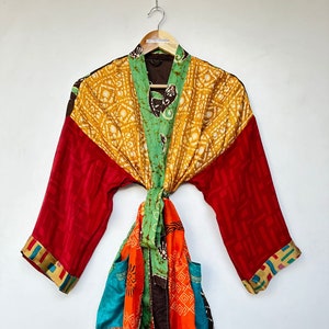 May include: A colorful patchwork kimono robe with a brown sash. The robe has a yellow, green, red, and orange pattern. The sash is tied at the waist.