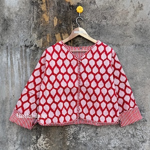 May include: Red and white cotton jacket with a leaf print and a button closure. The jacket has a V-neck and long sleeves with white stripes on the cuffs. The jacket is hanging on a wooden hanger.