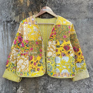 May include: A yellow quilted jacket with a floral print and a striped lining. The jacket has a V-neck and is made of cotton. The text "Hasthshilpam" is printed on the jacket.