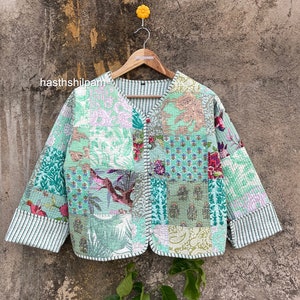 May include: A green quilted jacket with a patchwork design featuring floral and geometric patterns. The jacket has a V-neck, long sleeves, and a button closure. The text "hasthshilpam" is visible on the image.