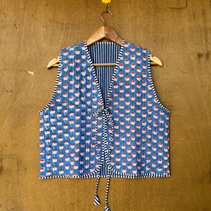 May include: A blue quilted vest with a floral print and a tie closure. The vest has a striped lining and a black trim.