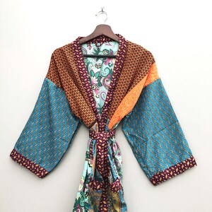 May include: A colorful, patterned robe with a tie closure. The robe features a mix of teal, orange, and brown fabrics with intricate designs. The sleeves are teal with a small repeating pattern, and the collar and trim are a darker brown.
