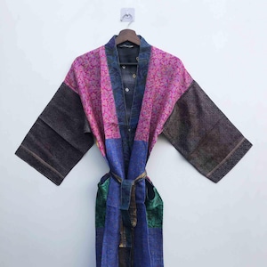 May include: A colorful robe with a floral pattern in pink and purple, with dark gray sleeves and a blue and green lower section. The robe is hanging on a wooden hanger against a white background.