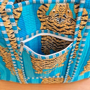 May include: A blue and white striped tote bag with a zippered pocket. The bag is made of quilted fabric and features a tiger print.