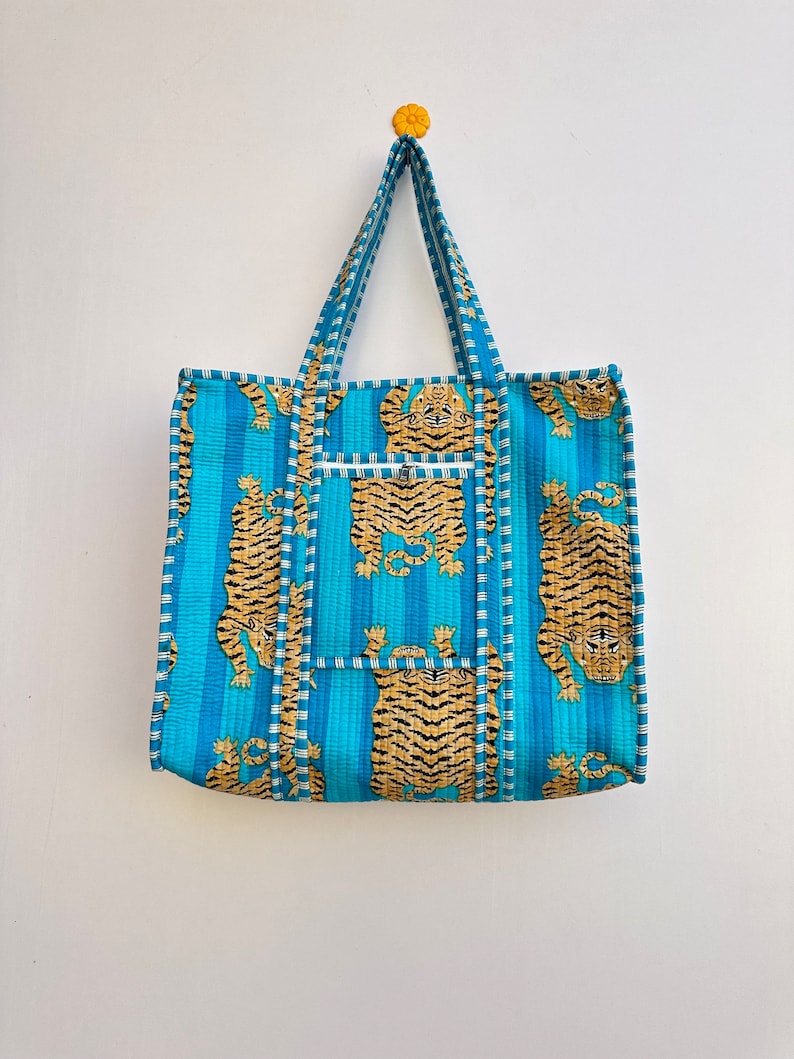 May include: A blue and orange tote bag with a tiger print. The bag has a zippered pocket on the front and two handles.