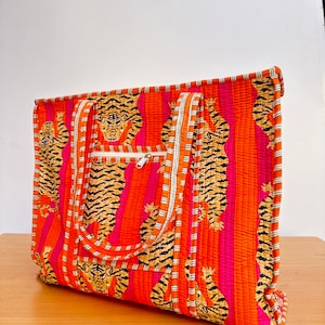 May include: A large orange and pink tote bag with a tiger print. The bag has two white straps and a zipper closure.