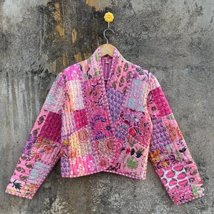Könnte beinhalten: Eine rosafarbene gesteppte Jacke mit Blumendruck. Die Jacke ist aus Patchwork-Stoff gefertigt und hat lange Ärmel.