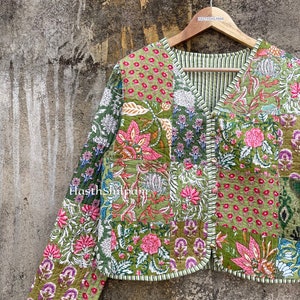 May include: A green quilted jacket with a patchwork design featuring floral patterns in shades of pink, green, and white. The jacket has a V-neck and a button closure. The text "Hasthshilpam" is visible on the jacket.
