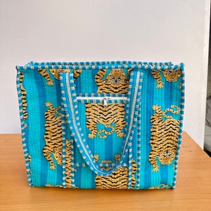 May include: A blue and white striped tote bag with a tiger print. The bag has two handles and a zippered pocket on the front.