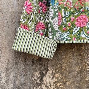 May include: A green and pink patchwork quilt with a floral print. The quilt has a striped green and white cuff. The quilt is made of cotton fabric.