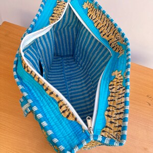 May include: A blue and white striped tote bag with a zipper closure. The bag is lined with a tiger print fabric.