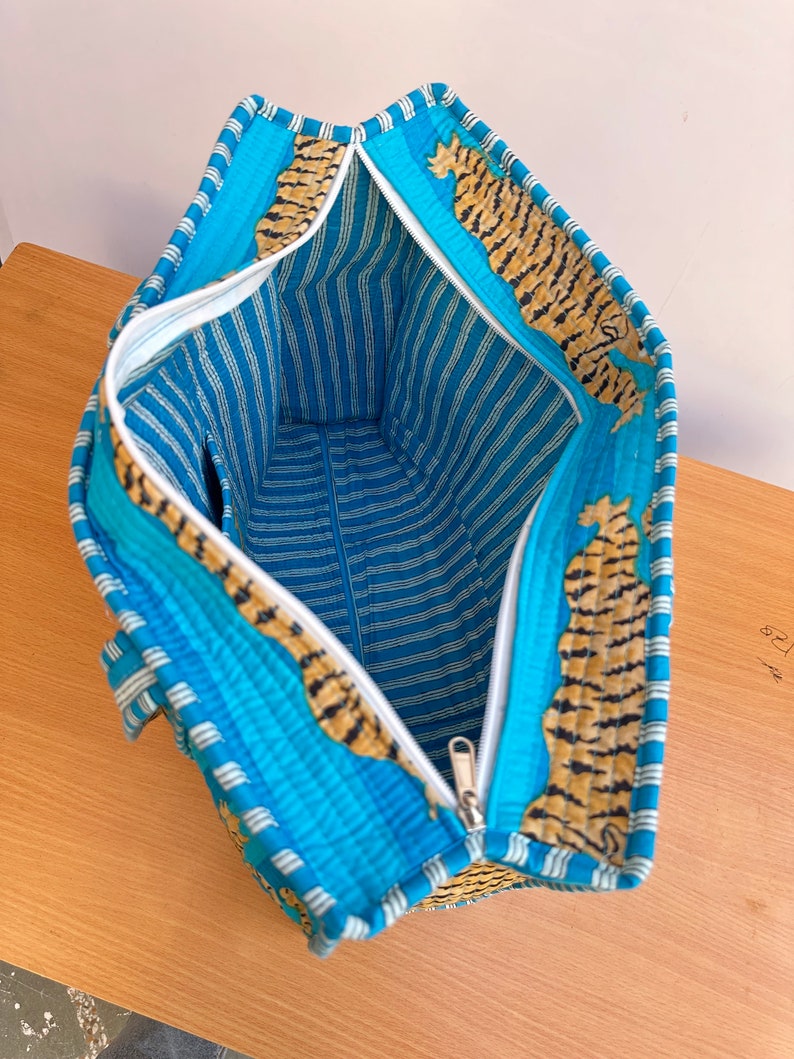 May include: A blue and white striped tote bag with a zipper closure. The bag is lined with a tiger print fabric.