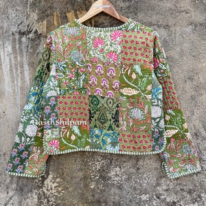 May include: A green quilted jacket with a patchwork design featuring floral and geometric patterns. The jacket has long sleeves and a round neckline. The text "Hasth Shilpam" is visible on the jacket.