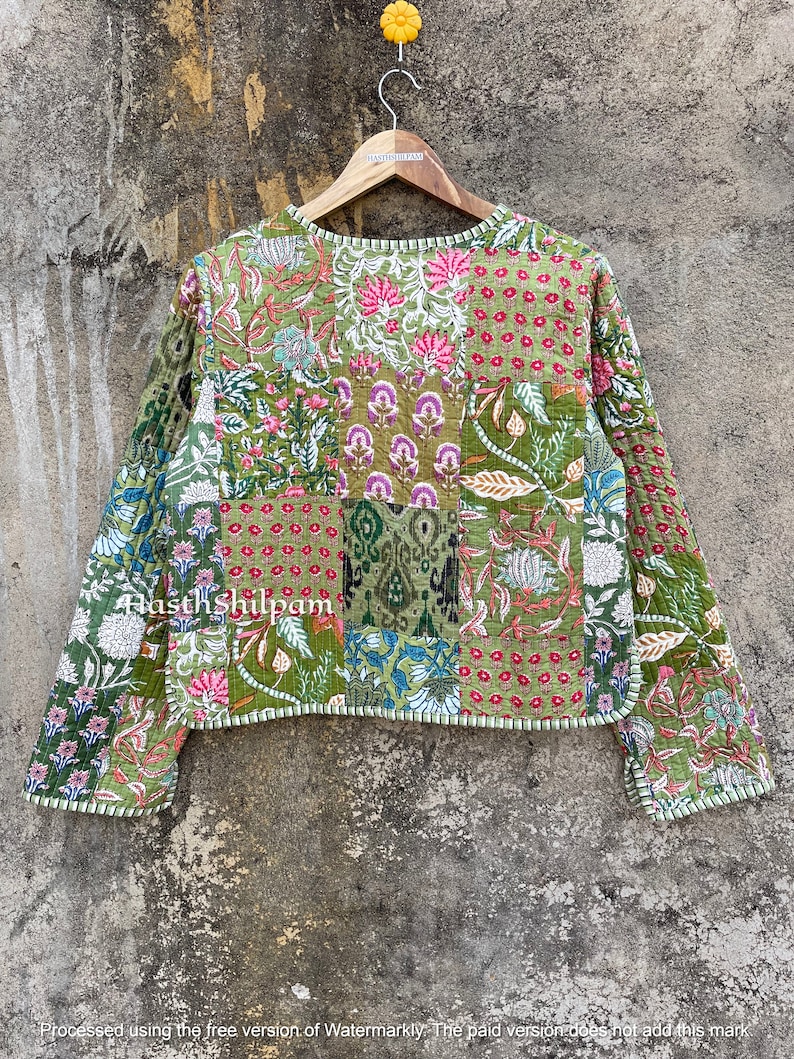 May include: A green quilted jacket with a patchwork design featuring floral and geometric patterns. The jacket has long sleeves and a round neckline. The text "Hasth Shilpam" is visible on the jacket.