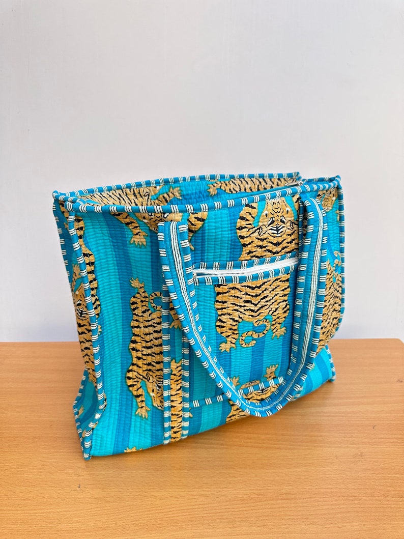 May include: A blue and white striped tote bag with a tiger print. The bag has two handles and a zipper closure.