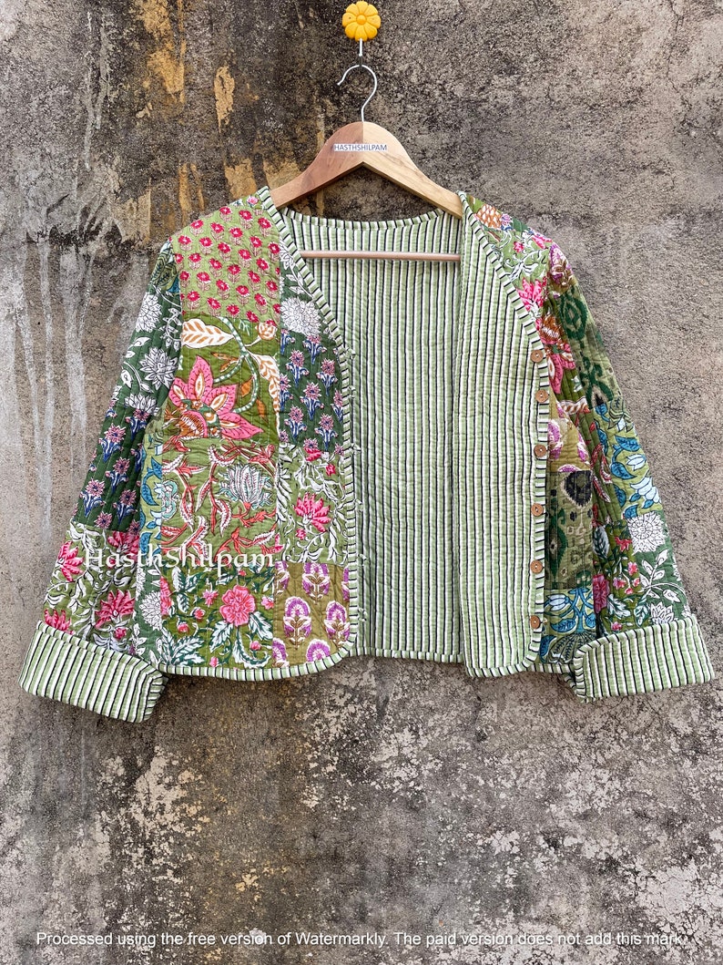 May include: A green quilted jacket with a floral print and striped lining. The jacket has a V-neck and is hanging on a wooden hanger.
