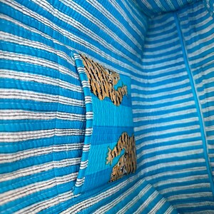 May include: The inside of a blue and white striped tote bag with a tiger print pocket. The pocket is sewn into the bag and is on the side of the bag.