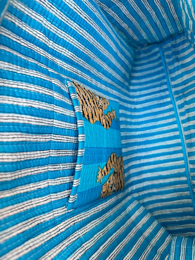 May include: The inside of a blue and white striped tote bag with a tiger print pocket. The pocket is sewn into the bag and is on the side of the bag.