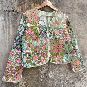 May include: A green quilted jacket with a floral print and a V-neck. The jacket has a button closure and long sleeves. The text "Hasth Shilpam" is visible on the jacket.