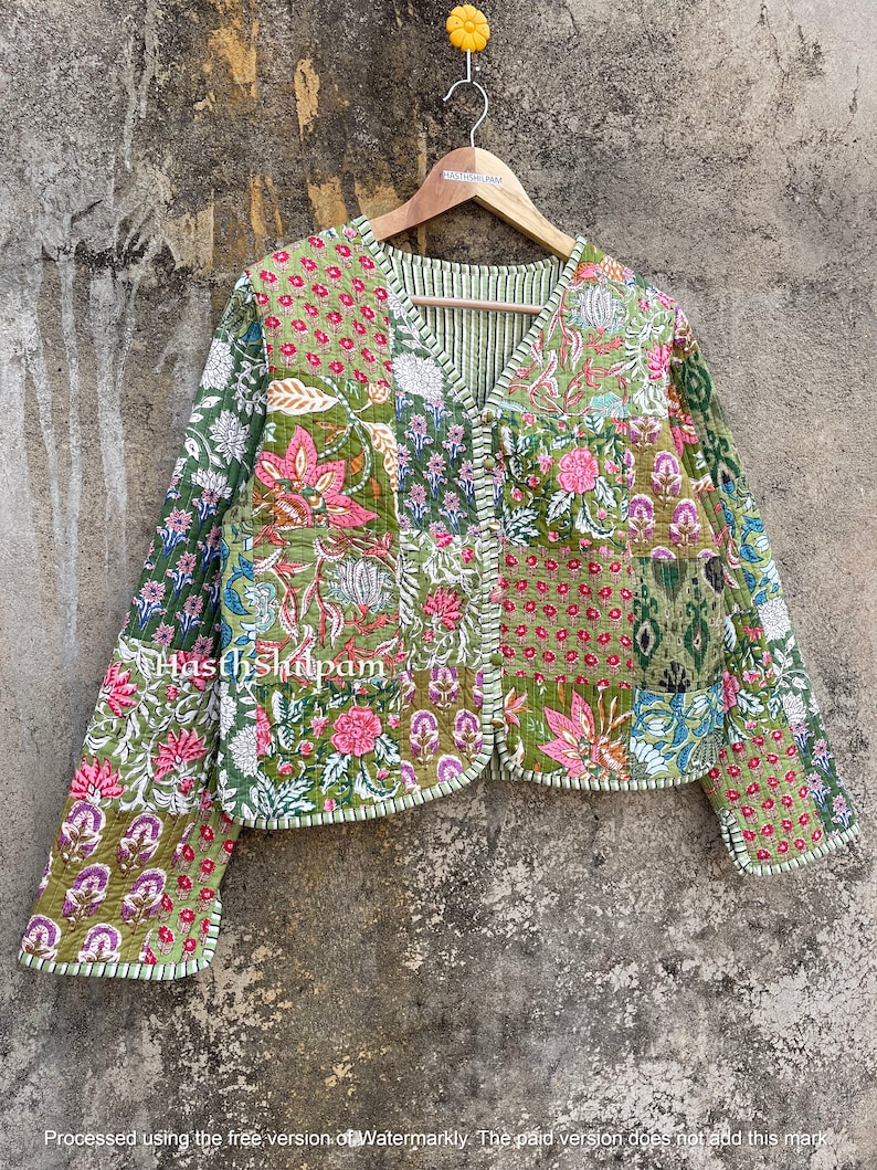 May include: A green quilted jacket with a floral print and a V-neck. The jacket has a button closure and long sleeves. The text "Hasth Shilpam" is visible on the jacket.