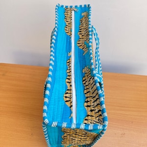 May include: A blue and orange tote bag with a zipper closure and tiger print fabric. The bag has white stripes around the edges.
