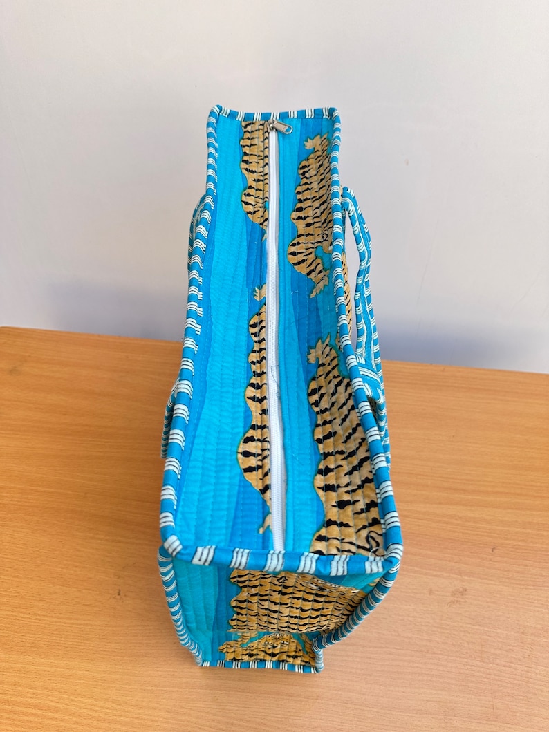 May include: A blue and orange tote bag with a zipper closure and tiger print fabric. The bag has white stripes around the edges.