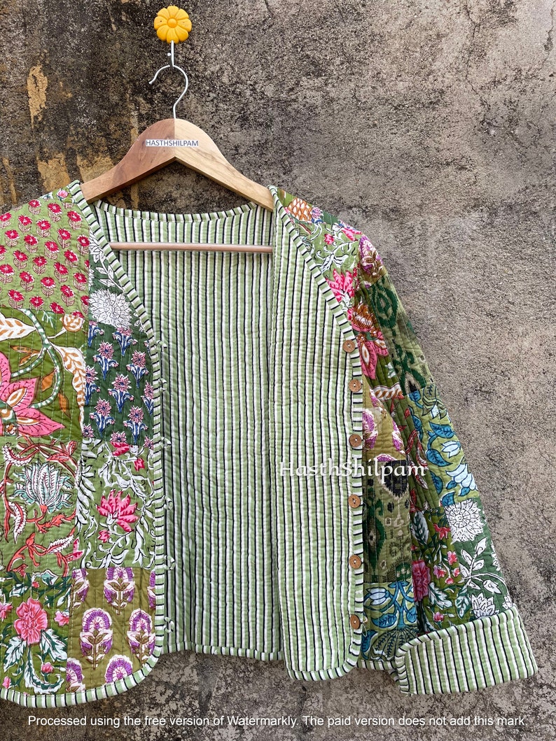 May include: A green quilted jacket with a floral print. The jacket has a striped lining and a button closure. The text "Hasthshilpam" is visible on the jacket.