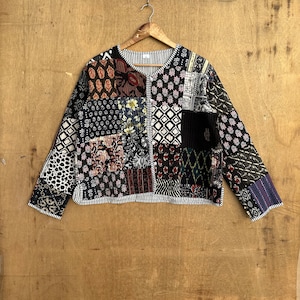 May include: A black and white patchwork quilted jacket with long sleeves. The jacket has a variety of floral and geometric patterns.