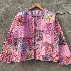 Może przedstawiać: Różowa pikowana kurtka z patchworkowym wzorem. Kurtka ma zapięcie na guziki i kołnierz. Tkanina jest miękka i wygodna.