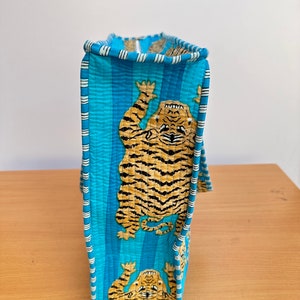 May include: A blue quilted tote bag with a white stripe pattern and a tiger print. The bag has a zipper closure and a top handle.
