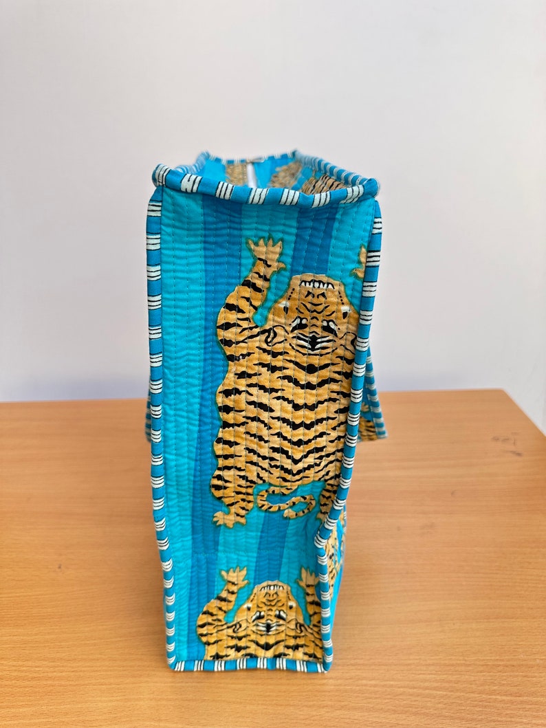 May include: A blue quilted tote bag with a white stripe pattern and a tiger print. The bag has a zipper closure and a top handle.