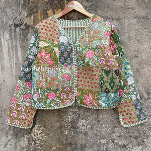 May include: A green quilted jacket with a floral print and a V-neck. The jacket has a button closure and long sleeves. The fabric is patchwork and has a textured surface.