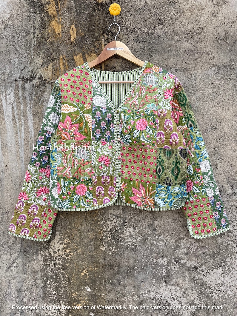 May include: A green quilted jacket with a floral print and a V-neck. The jacket has a button closure and long sleeves. The fabric is patchwork and has a textured surface.